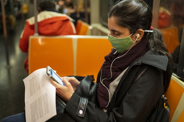 A woman wearing a mask uses her iPhone device while riding the subway.